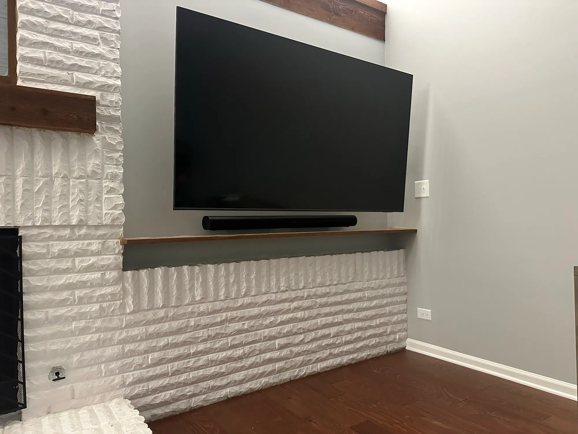 Television mounted on a painted white brick wall above a reclaimed wood ledge, with a soundbar beneath.