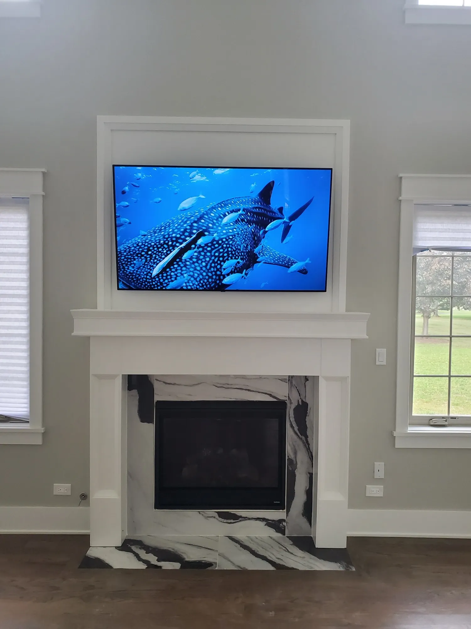 Television recessed into white millwork directly above a marble-surround gas fireplace.