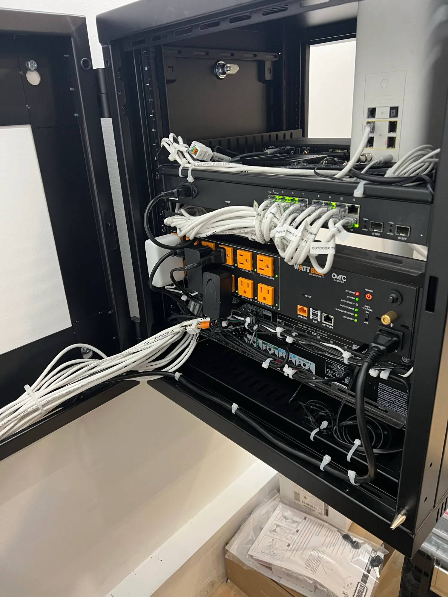 Open structured wiring enclosure with Cat6 runs dressed and tied, a labeled network switch, and a rack-mounted power conditioner.